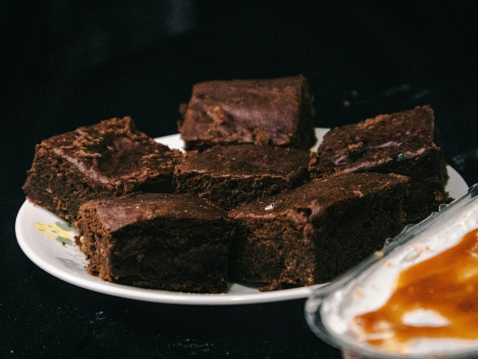 Six square chocolate brownies on a white plate with dark background. Photo by Azmaan Baluch on Unsplash https://unsplash.com/photos/chocolate-cake-on-white-ceramic-plate-BJsYX2m5hBc