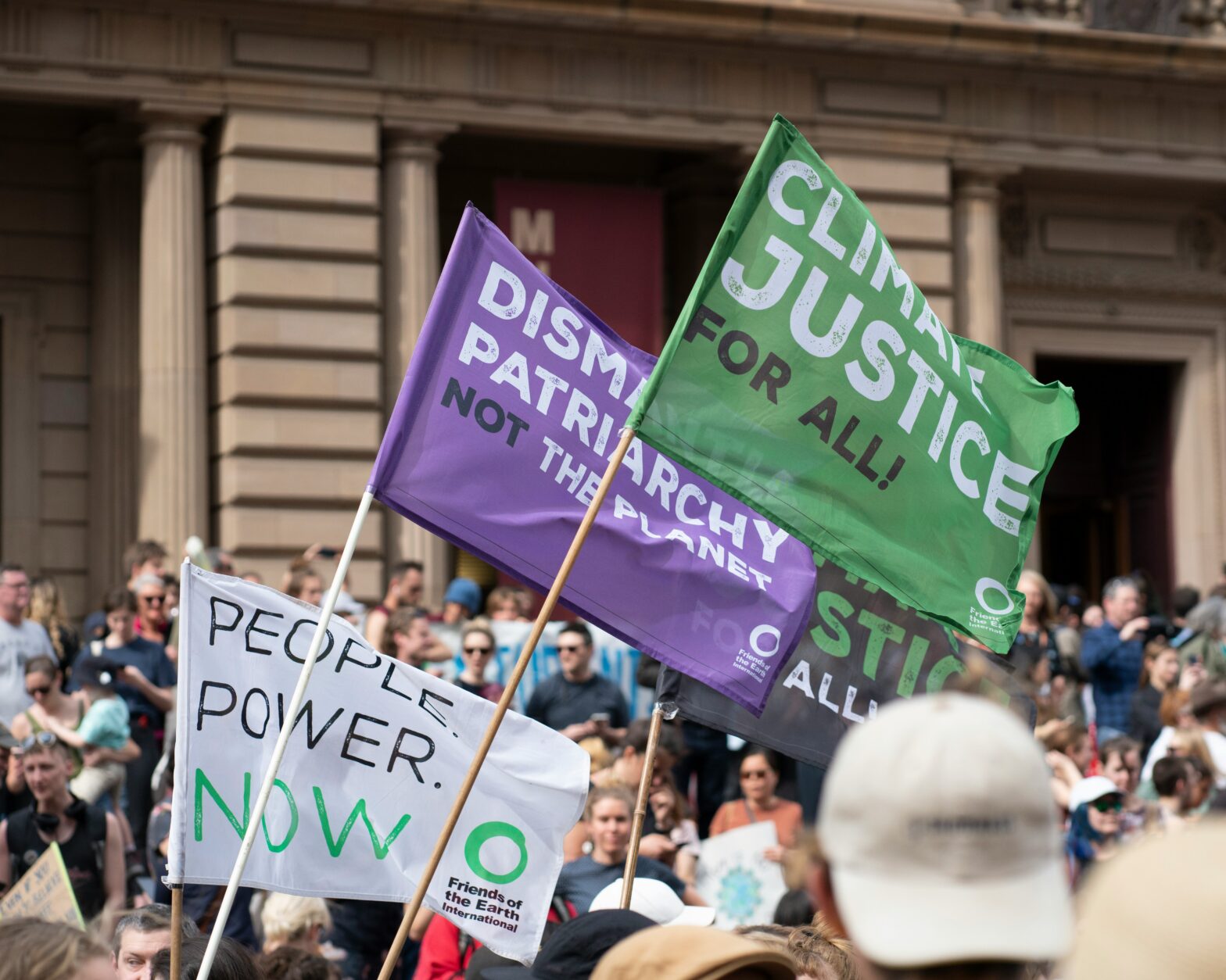Protestors with banners bearing climate justice slogans outside a government building. Photo by Lawrence Makoona on https://unsplash.com/photos/a-group-of-people-holding-signs-in-front-of-a-building-o_OMiYzkJMI Unsplash