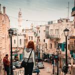 A woman standing on a street in the town of Bethlehem, Palestine. Photo by Jonas Brief https://unsplash.com/photos/woman-wearing-gray-and-white-hoodie-standing-near-black-lampposts-iYNxGJsb57s Unsplash