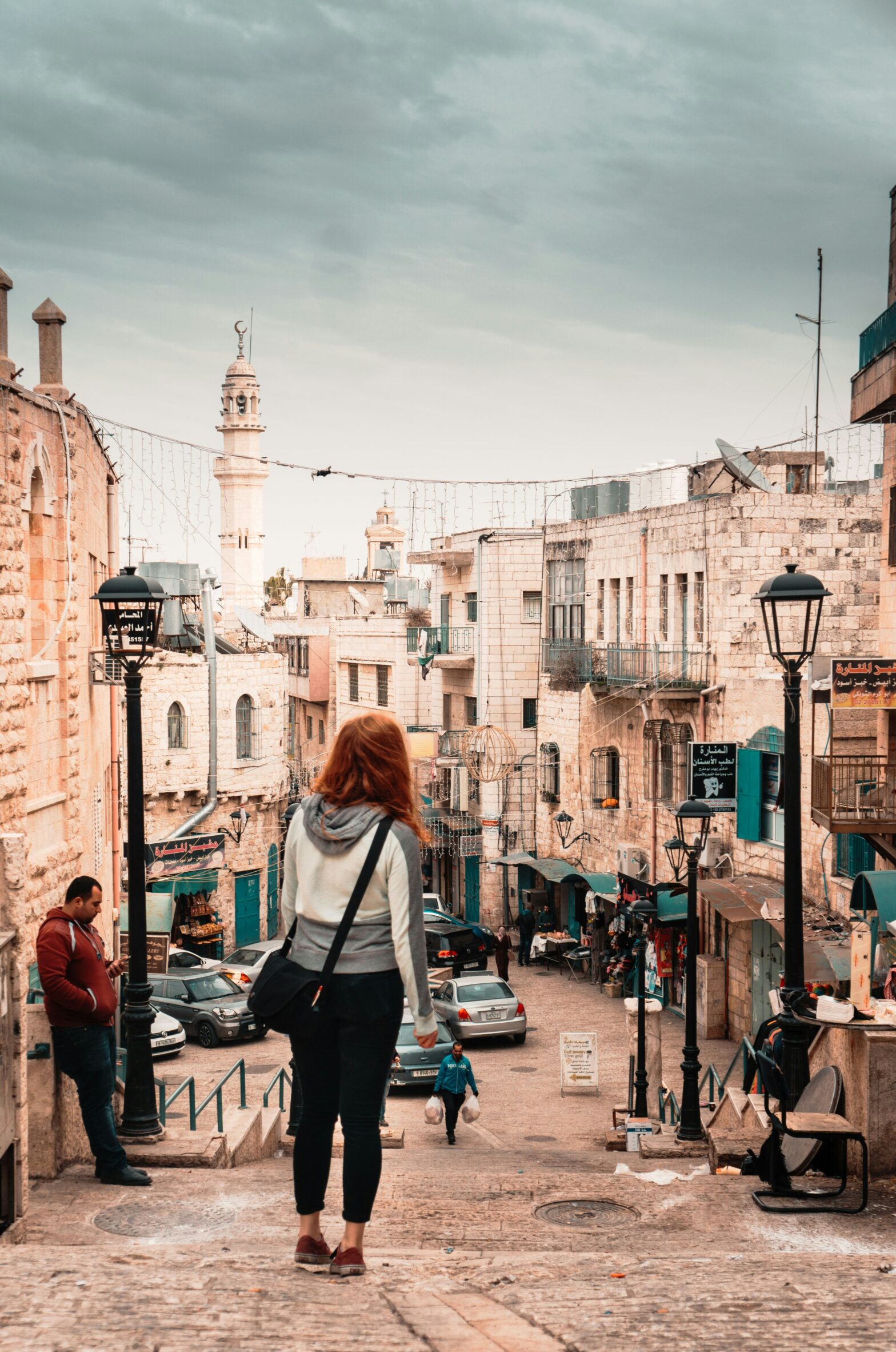 A woman standing on a street in the town of Bethlehem, Palestine. Photo by Jonas Brief https://unsplash.com/photos/woman-wearing-gray-and-white-hoodie-standing-near-black-lampposts-iYNxGJsb57s Unsplash